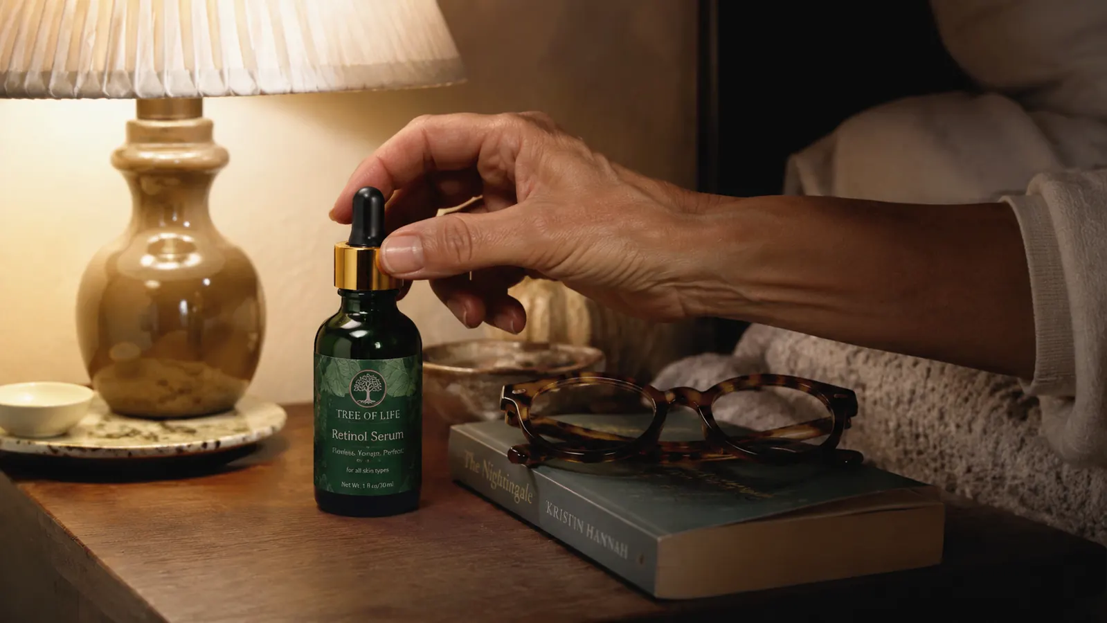 Close-up of the Tree of Life retinol serum bottle on a nightstand next to a glass of water and reading glasses